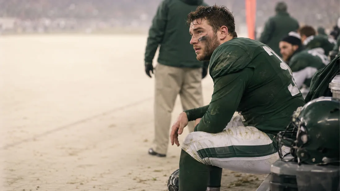 A football player resting on the sideline, uniform stained with mud late in the game